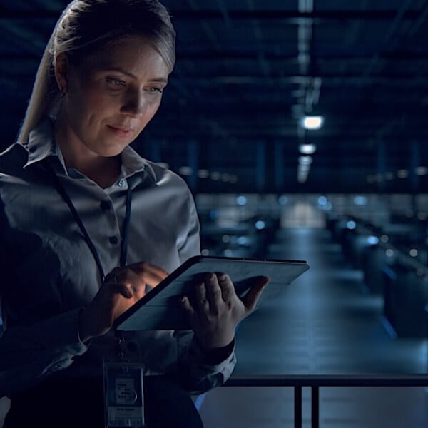 Frau mit Tablett vor einer Produktionshalle, füllt einen digitalen Arbeitsauftrag in der Flow360-Software aus.